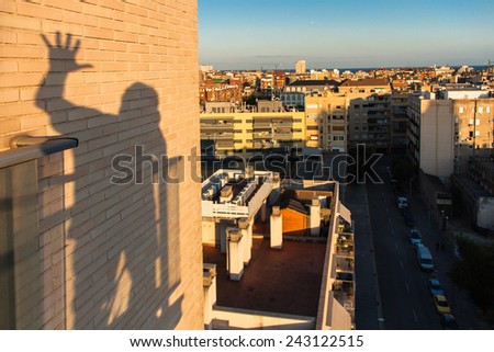 Shadow on the wall of a man silhouette waving hello. City view from a terrace.