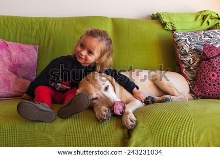 Two year old girl and a Labrador Retriever at the sofa at home