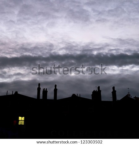 Row of old town houses silhouetted against evening sky; single lit window; excellent copy-space