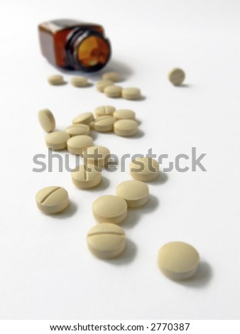 yellow tablets spilling from brown medicine bottle; differential focus