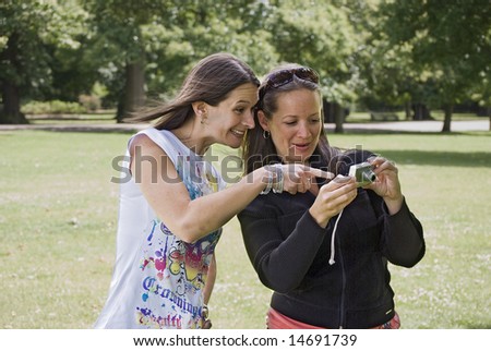two pretty young women laughing over a picture on a compact camera in the park