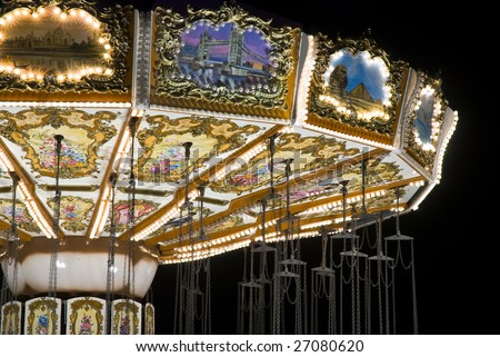detail of brightly-lit chair-o-plane fairground ride, showing traditional fairground artwork, against pure black sky
