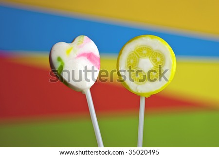 two lollipops (one heart-shaped, one decorated with lemon slices) against colorful background