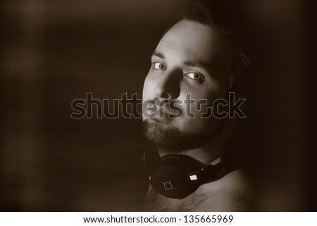 vintage-like low key portrait of young man with beard and hairy shoulders in headphones