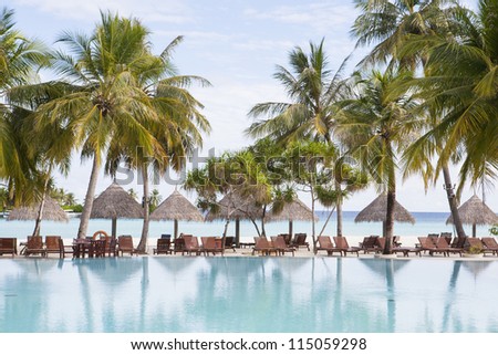 tropical beach with palms and sun shade behind the swimming pool of a holiday resort