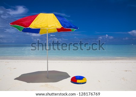 a red, yellow blue and green sunshade and a swimming ring at the beach with a turquoise sea
