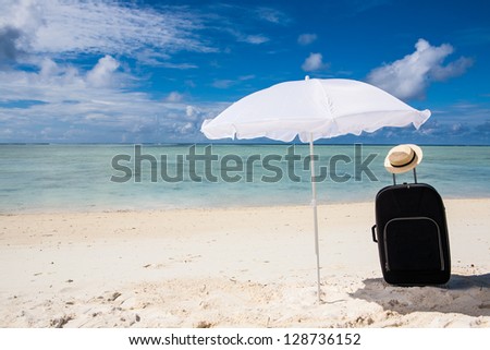 black suitcase sun hat and white sunhade at the beach