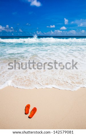 orange flip-flops at the beach with a turquoise sea under a deep blue sky with white clouds