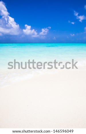 background of a white sandy beach with a turquoise sea under a deep blue sky with some white clouds