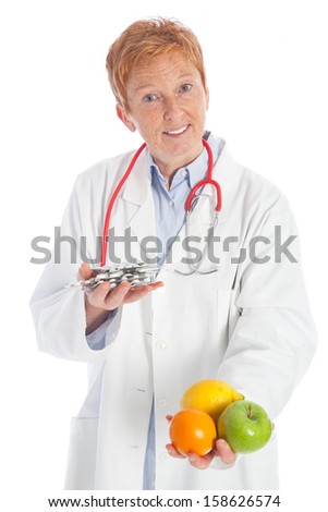 elder female practitioner doctor with a red stethoscope and a white doctorÃ?Â´s overall holding fruits and pills in her hands, offering healthy food or medicine to choose