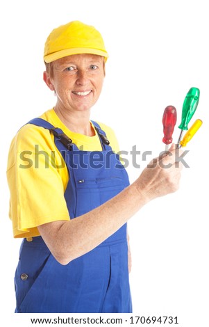 portrait of a female mechanic worker with a yellow cap and a blue bib overall holding three screw drivers in one hand in front of a white background