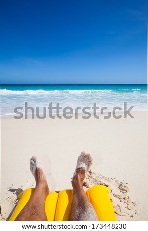 legs and feet of a man, sunbathing on a yellow air mattress at a beautiful beach with a turquoise sea and a blue sky, Seychelles, Africa