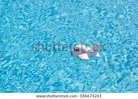 travel background of a toy airplane floating in the rippled blue water of a blue swimming pool