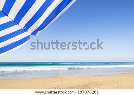 travel background with a blue and white sunshade at an endless white beach with a blue sky and a turquoise sea,  Playa de las Pilas, Fuerteventura, canary islands, Spain, Europe