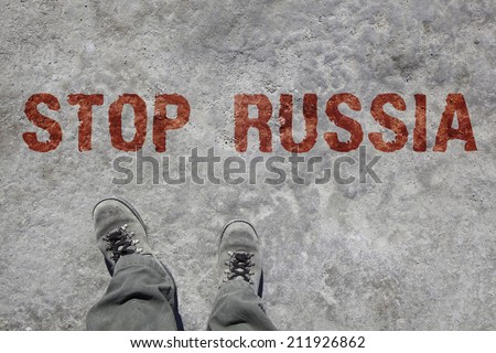 man in grey military boots and pants is looking down to his feet. On the stony ground is written STOP RUSSIA in red color.