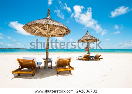 beautiful tropical beach with green coconut palms straw sunshades and wooden sunbeds in front of a turquoise sea with a blue sky, Mauritius, Africa