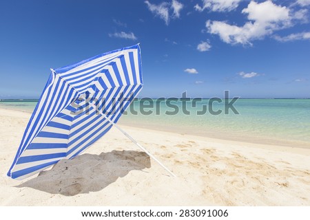 blue and white colored sunshade in the white sand of a beautiful beach with a blue sky and turquoise sea, Mauritius, Africa