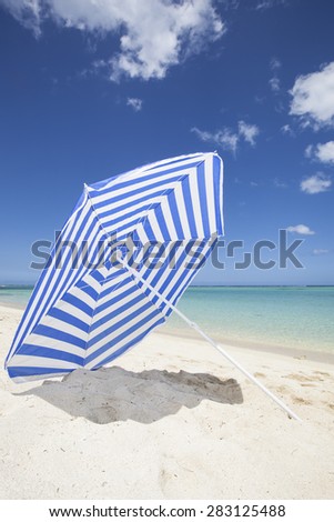 blue and white colored sunshade in the white sand of a beautiful beach with a blue sky and turquoise sea, Mauritius, Africa