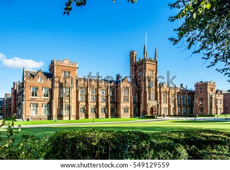 The Queen\'s University of Belfast with a grass lawn, tree branches and a hedge in sunset light