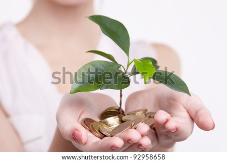 woman's hands holding plant sprouting from a handful of coins