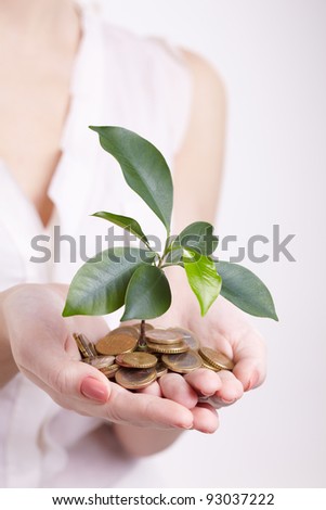 woman\'s hands holding plant sprouting from a handful of coins