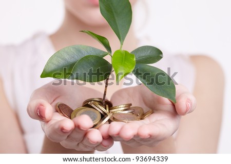 woman's hands holding plant sprouting from a handful of coins