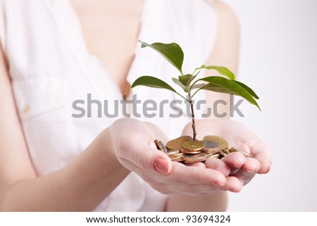 woman\'s hands holding plant sprouting from a handful of coins