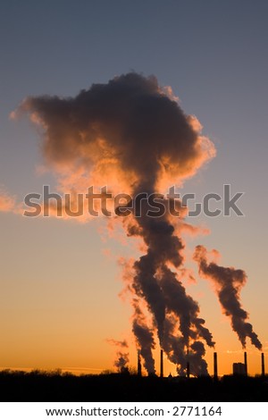 Silhouette of smoke stacks smoking into the sky at sunset