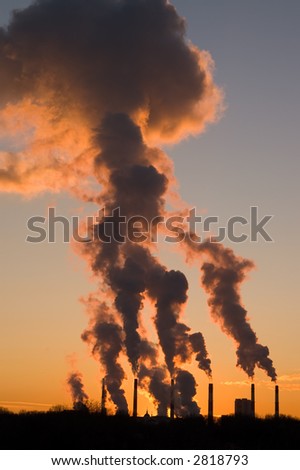 Silhouette of smoke stacks smoking into the sky at sunset