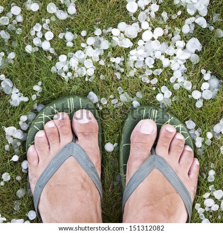 Man with flip-flops standing on the grass with hails after hailstorm