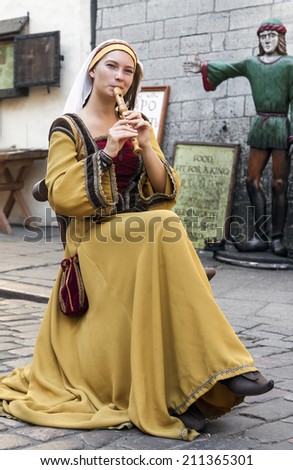 TALLINN, ESTONIA - JULY 31, 2014: Young girl in traditional costume playing flute in Tallinn old town, Estonia.