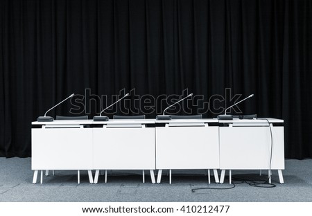 Monochrome picture of conference stand table with microphones in a meeting room