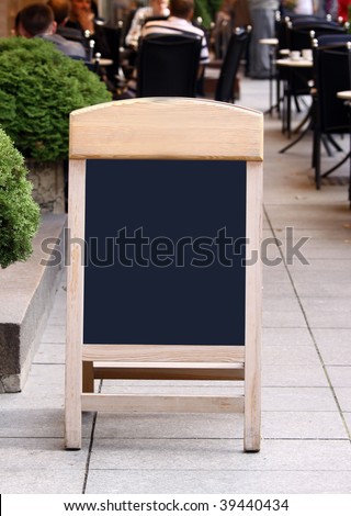Empty menu board standing on the street and people seen eating on the blurred background
