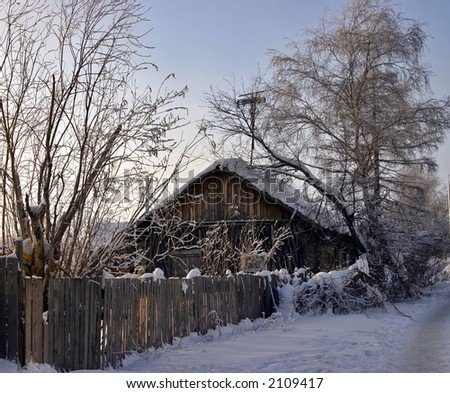 snow-capped log cabin in surroundings trees and fence on a background clear sky