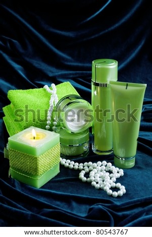 Creams for body care, candles and a green towel on a dark blue glossy velvet