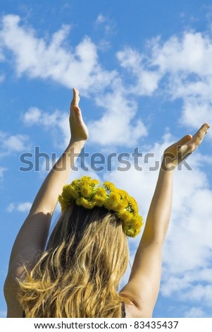 girl in a wreath from flowers with the hands lifted to the blue sky