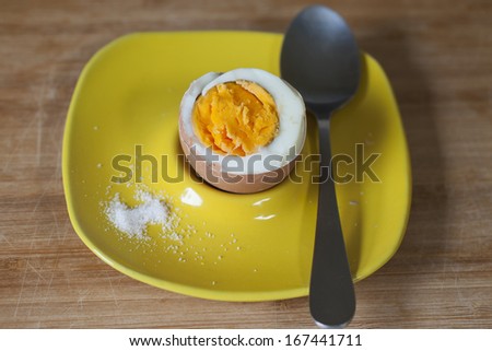 Hard boiled hen egg on yellow plate with spoon an salt.