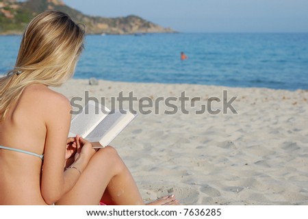 a blonde girl reads a book while sitting on the beach. Blue sea on the background