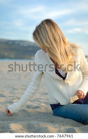 stock photo : a girl with long blonde hair is searching some seashells on a 