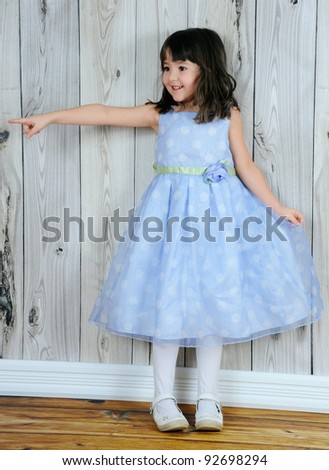 happy little girl in beautiful blue dress pointing at something