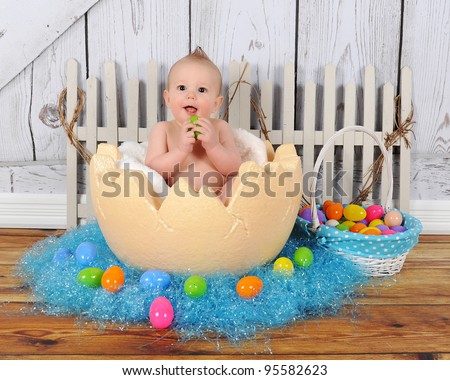 adorable baby boy sitting in giant easter egg surrounded by colourful Easter grass and eggs
