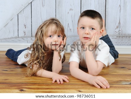 young brother and sister laying together in floor with hands on chin