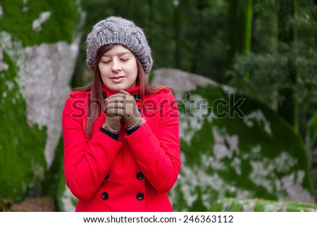 Young woman shivering with cold on a forest wearing a red overcoat, a beanie and gloves during winter