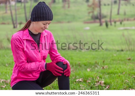 Young athlete woman hurting from a knee injury on a cold winter day in the track of an urban park.