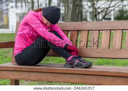 Young athlete woman tired or depressed resting on a bench on a cold winter day in the track of an urban park.