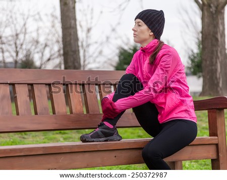 Sad young female athlete sitting on a bench on a cold winter day in the track of an urban park.