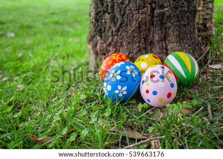 Painted Easter eggs hidden on the grass behind a tree trunk, ready for the easter egg hunt traditional play game