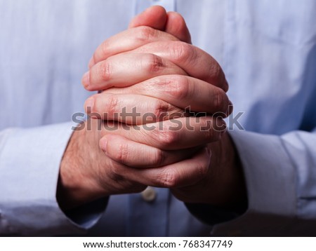 Close up or closeup of hands of faithful mature man praying. Hands folded, interlaced fingers in worship to god. Concept for religion, faith, prayer and spirituality.