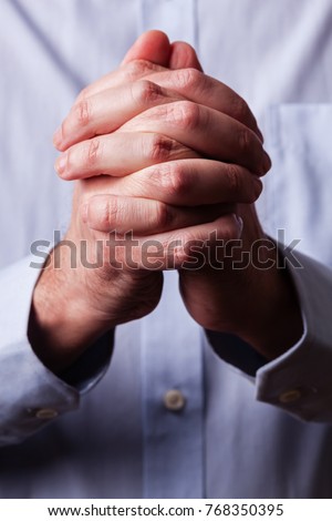 Close up or closeup of hands of faithful mature man praying. Hands folded, interlaced fingers in worship to god. Concept for religion, faith, prayer and spirituality.