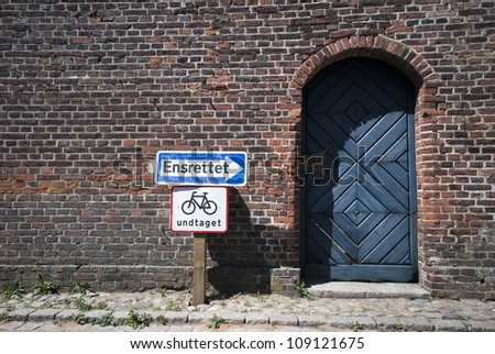 Traffic signs outside old brick wall and blue door in Ribe, Denmark